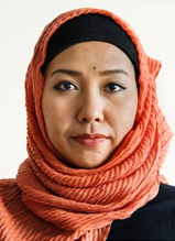 Woman from the neck up wearing a hijab in front of a light-colored background.